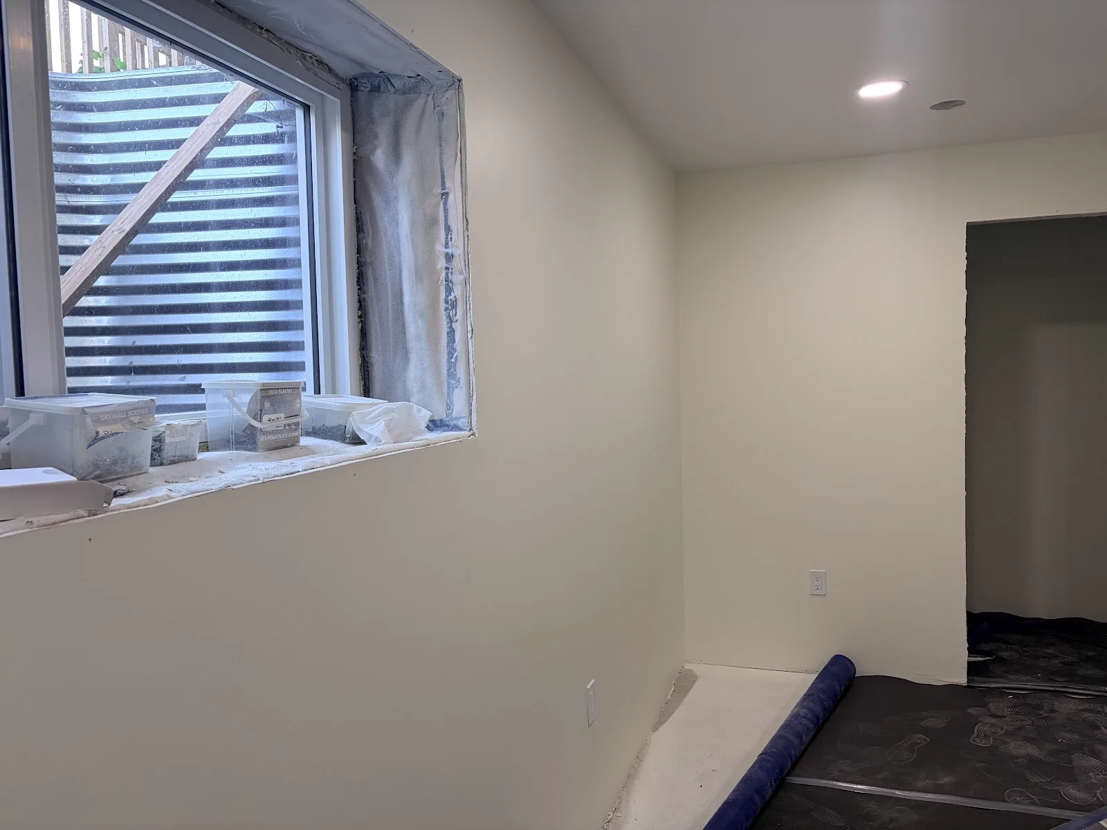 Basement room mid-project with fresh primer and floor protection in place